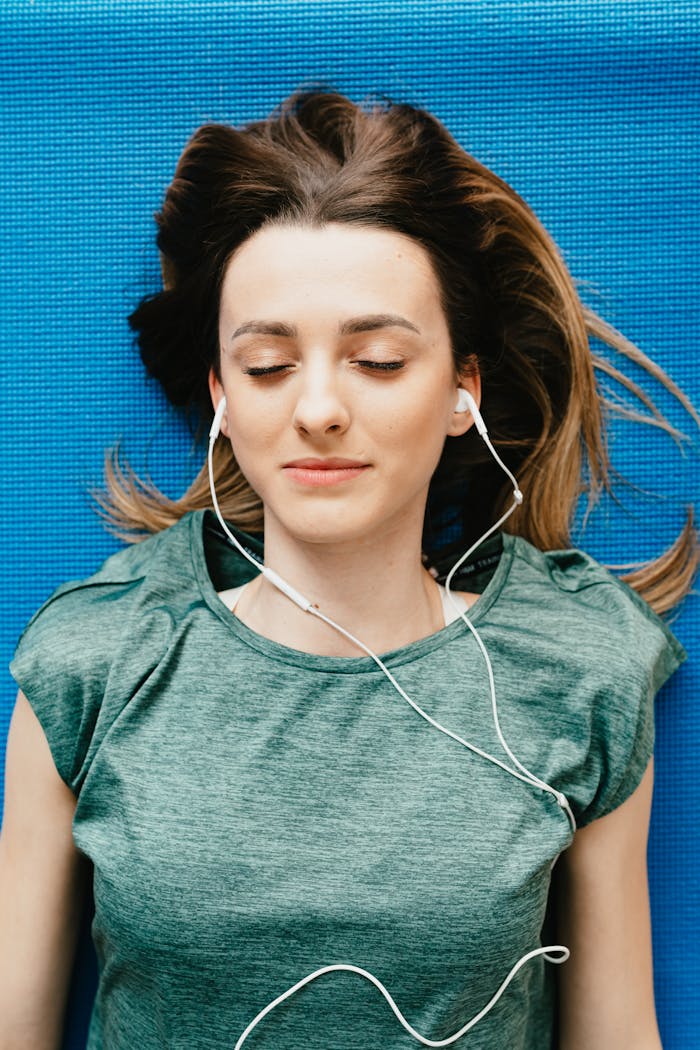 Young woman lying on yoga mat with earphones, eyes closed in relaxation.