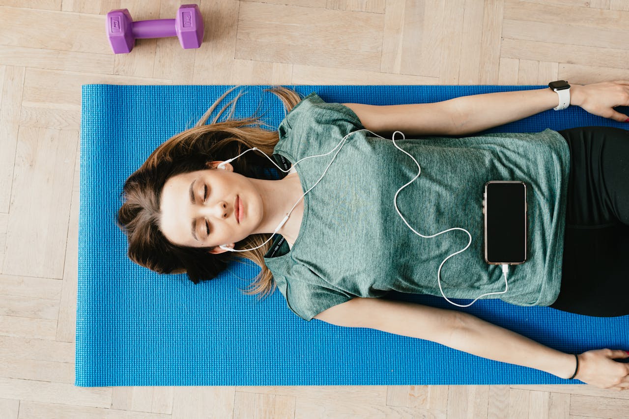 Young woman lying on a yoga mat listening to music for relaxation and mindfulness.
